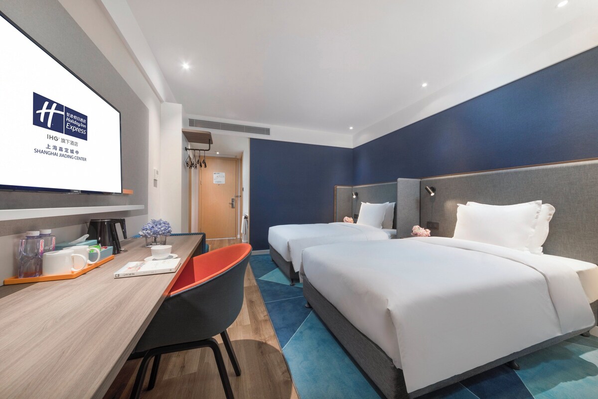Habitació d'hotel amb dos llits, un escriptori amb una cadira, una pantalla de televisió i una porta al bany.