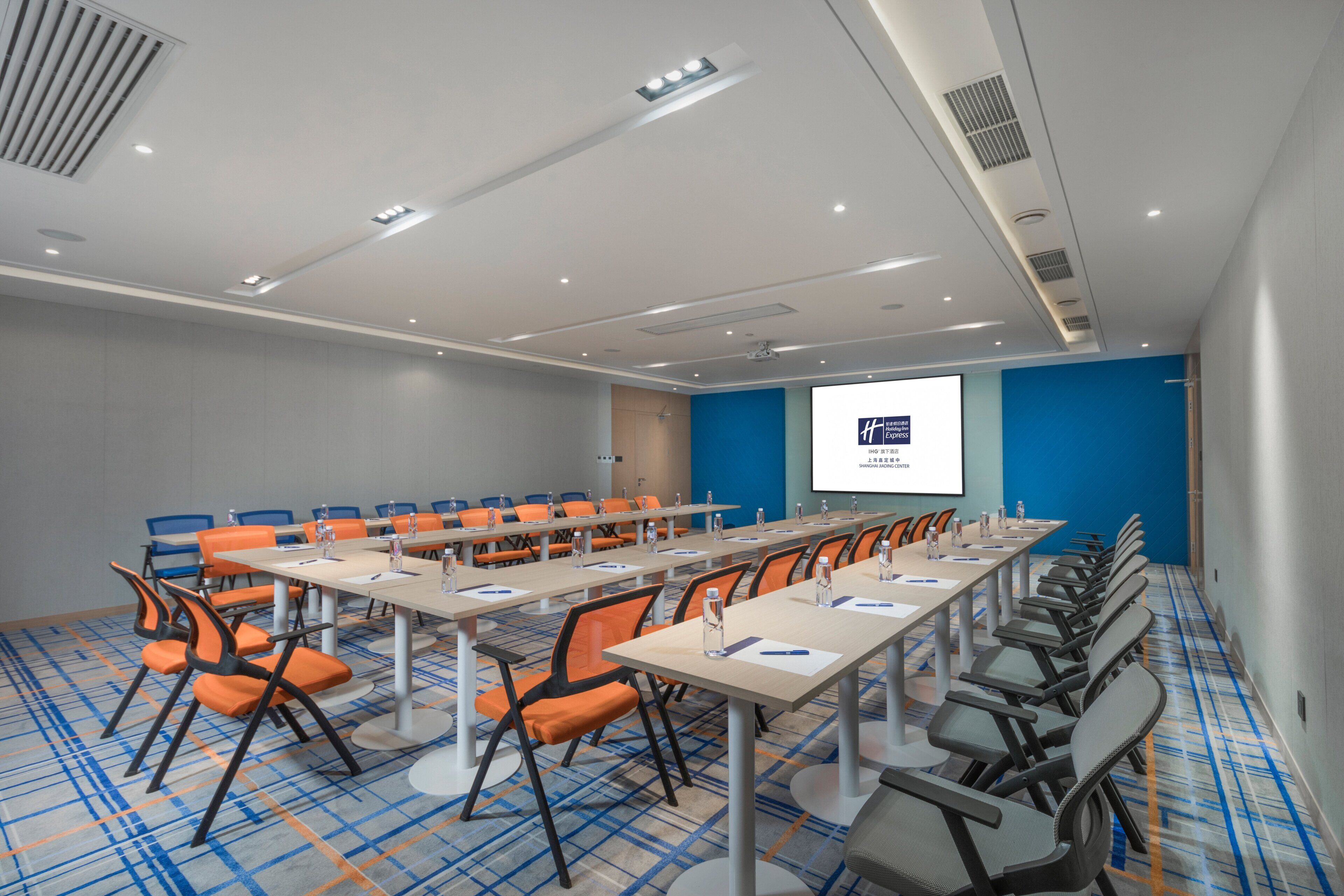A conference room with a long table, multiple chairs, and a projector screen displaying a presentation.