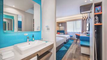 A hotel room with a large bathroom sink, a mirror, a bed, a desk, and a shower area.