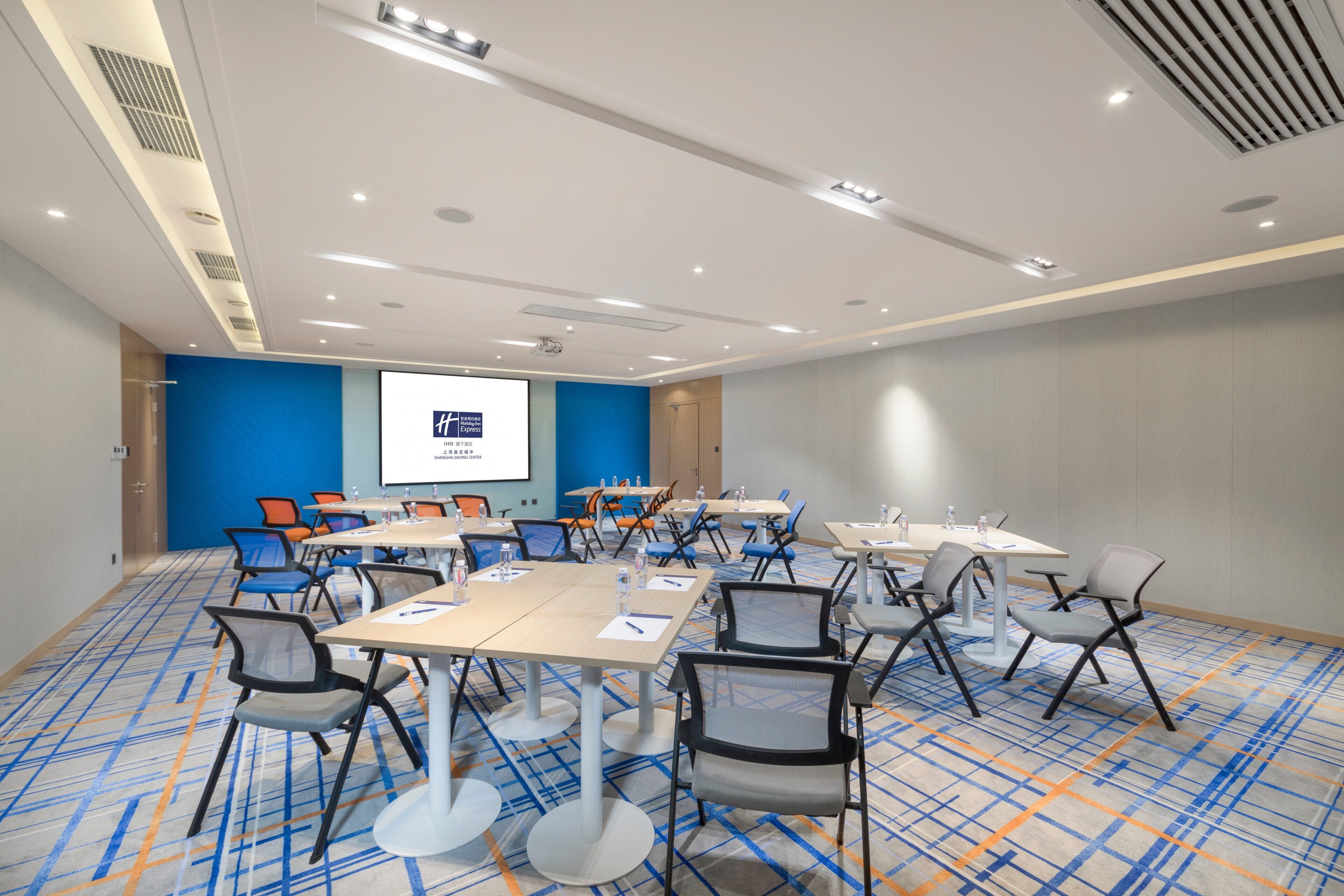 Un salón de conferencias con varias mesas y sillas, una pantalla de proyector y una pared de acento azul.