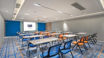 A conference room with multiple tables and chairs, a projector screen, and a presentation on the wall.
