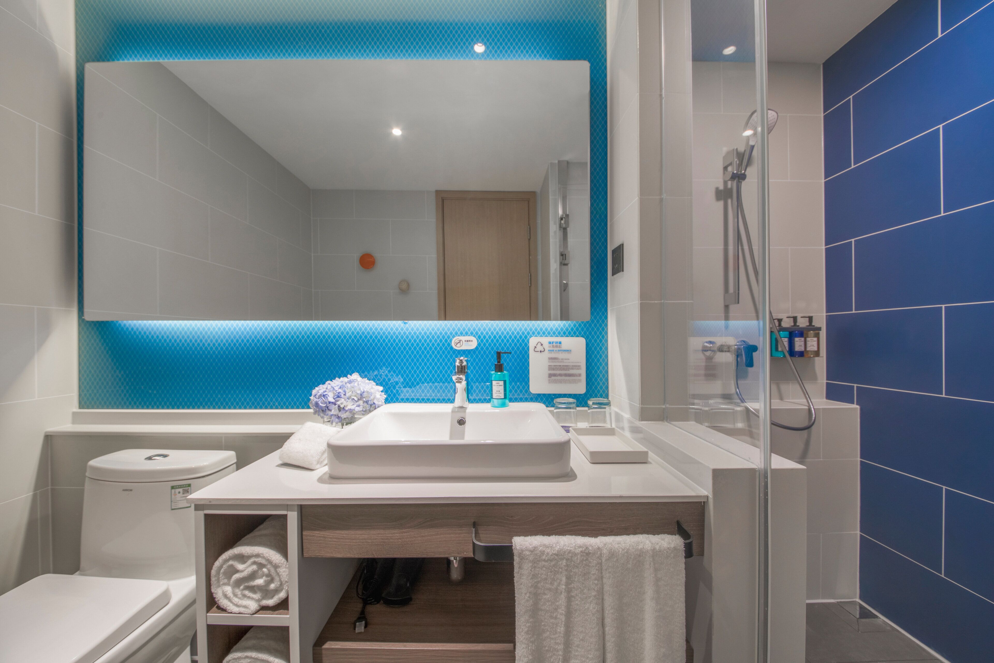 Un baño moderno con un espejo grande, lavamanos blanco y zona de ducha.