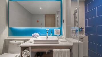 Un baño moderno con un espejo grande, lavamanos blanco y zona de ducha.