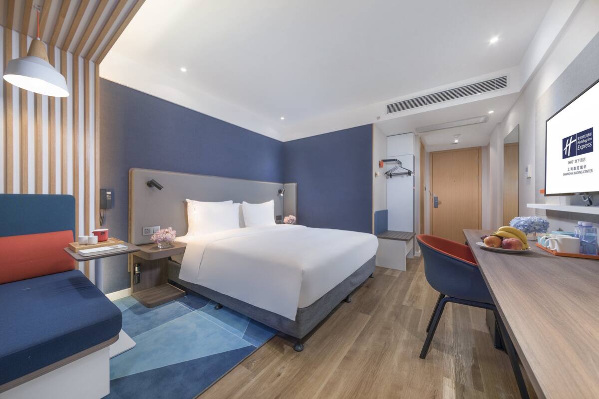 A modern hotel room with a large bed, a desk, and a seating area.