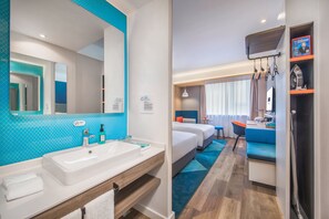 Habitació d'hotel moderna amb un bany gran, un lavabo, un mirall, un llit amb roba de llit blava, un escriptori amb una cadira i una televisió.