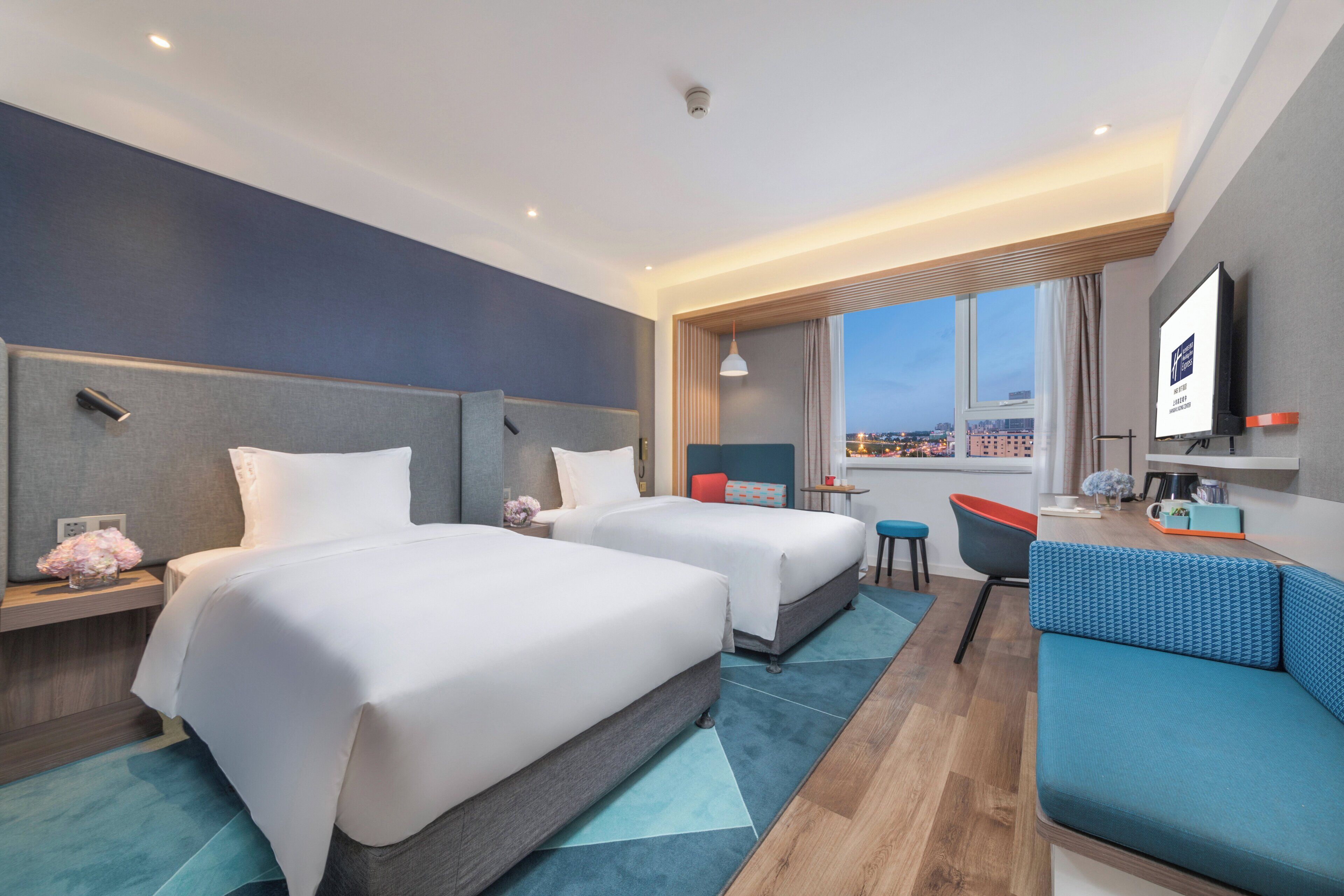 Een hotelkamer met twee bedden, een bank, een televisie en uitzicht op de stad.
