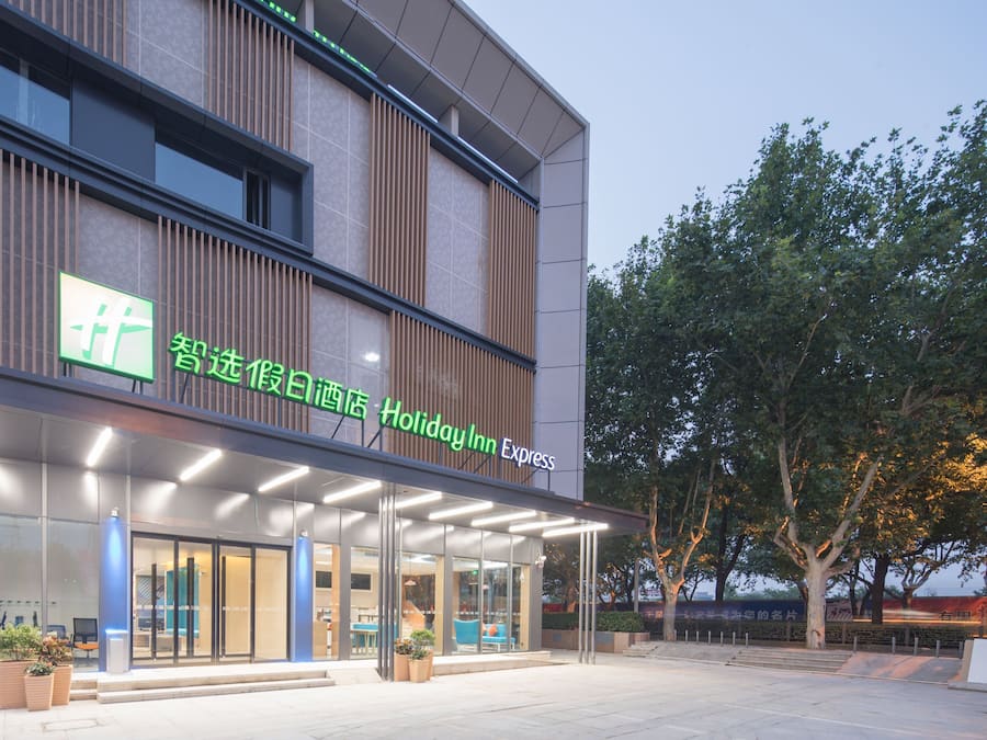 A modern hotel with a glass facade, outdoor seating, and a sign for Holiday Inn Express.