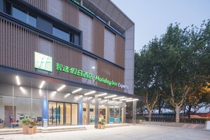 Een modern hotel met een glazen gevel, buiten zitplaatsen en een bord met Holiday Inn Express.
