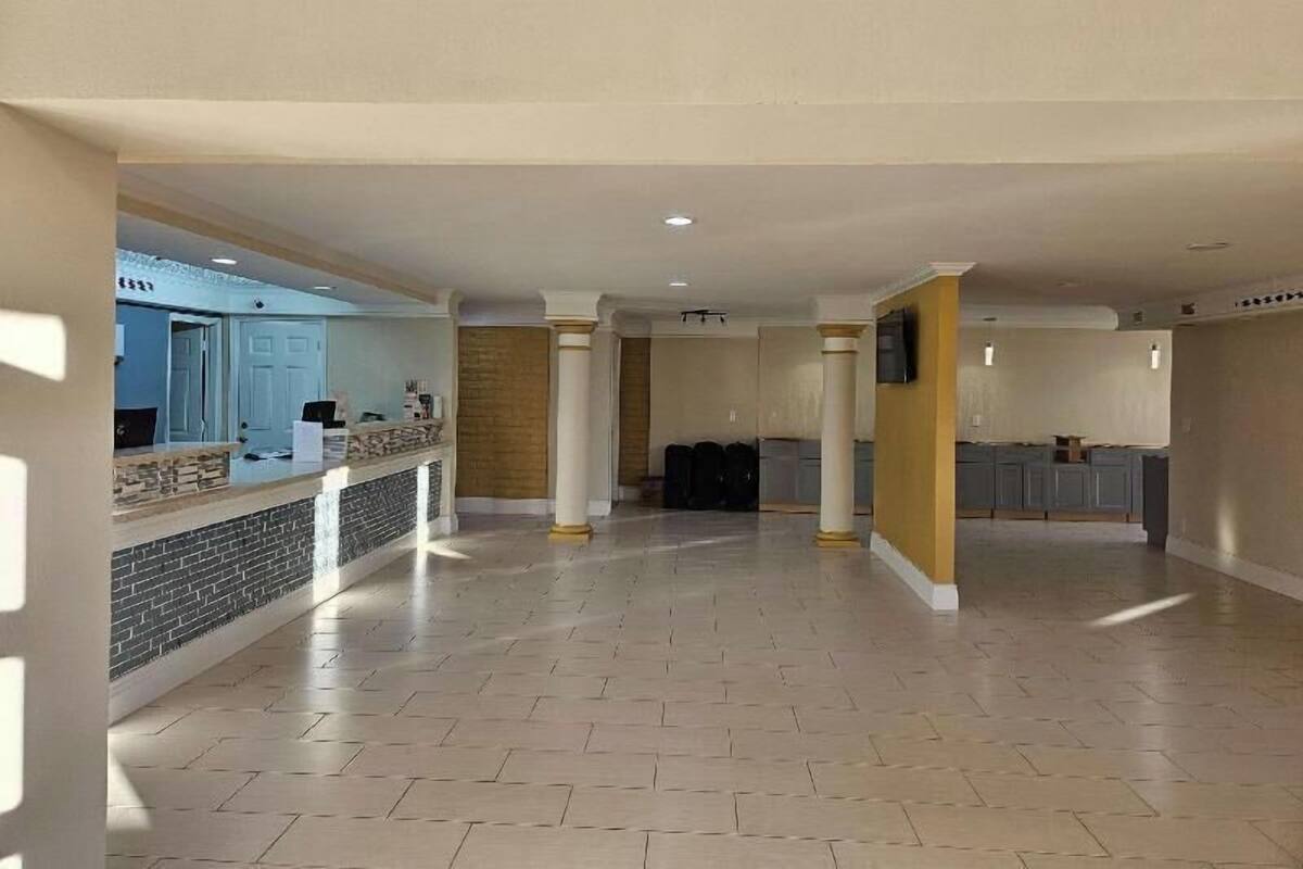 A spacious lobby with a reception desk, columns, and a kitchen area in the background.