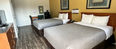 Habitación de hotel con dos camas, un escritorio, una silla, un televisor y obras de arte en las paredes.