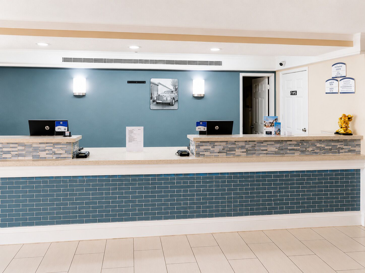 A reception desk with two HP computers, a blue wall, a tiled floor, and a door with a sign.
