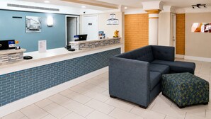 A reception area with a counter, a laptop, a sofa, and a patterned ottoman. - Baymont by Wyndham Nacogdoches Near University (Nacogdoches)