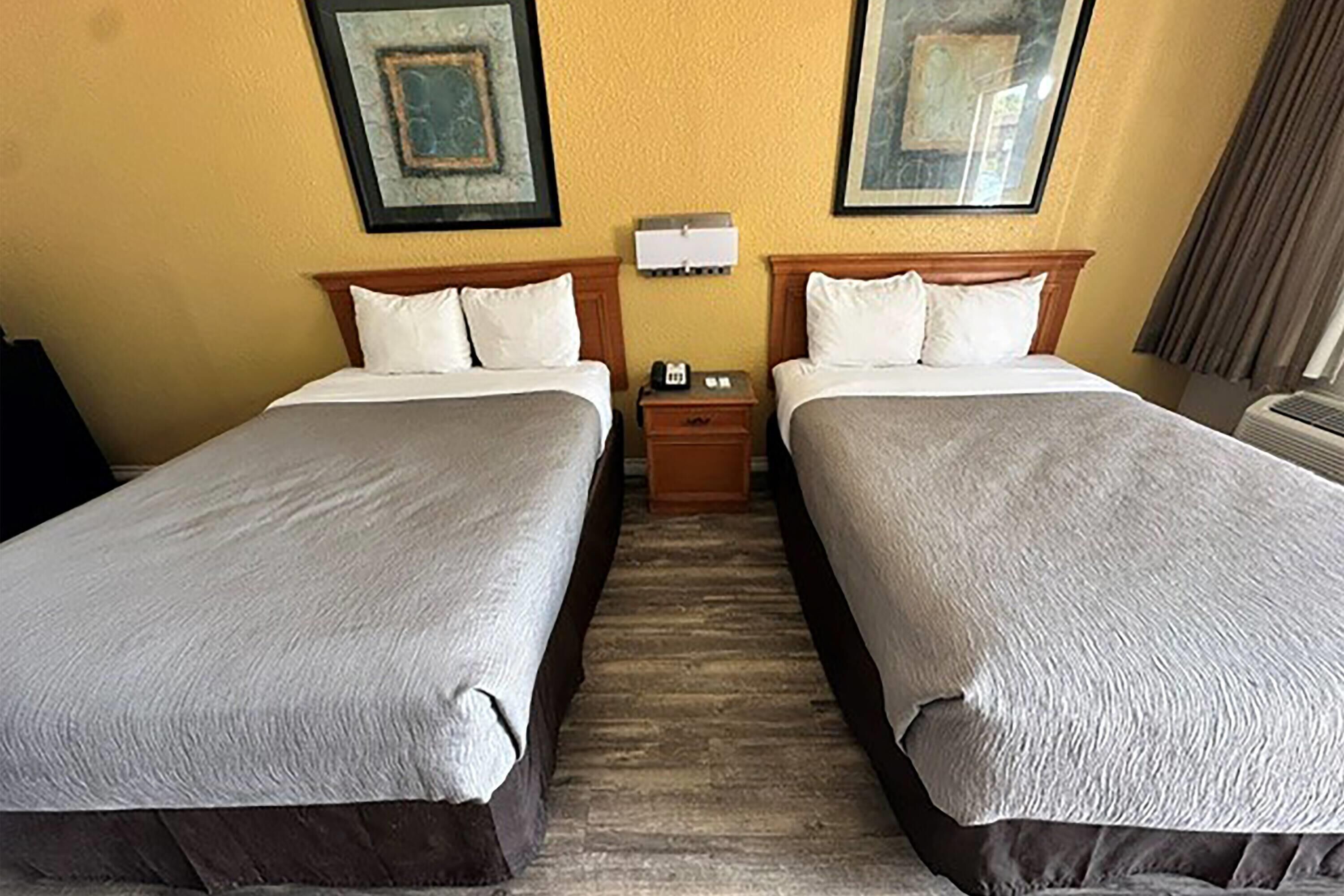 A hotel room with two beds, a nightstand, a wall-mounted phone, and framed artwork on the wall.