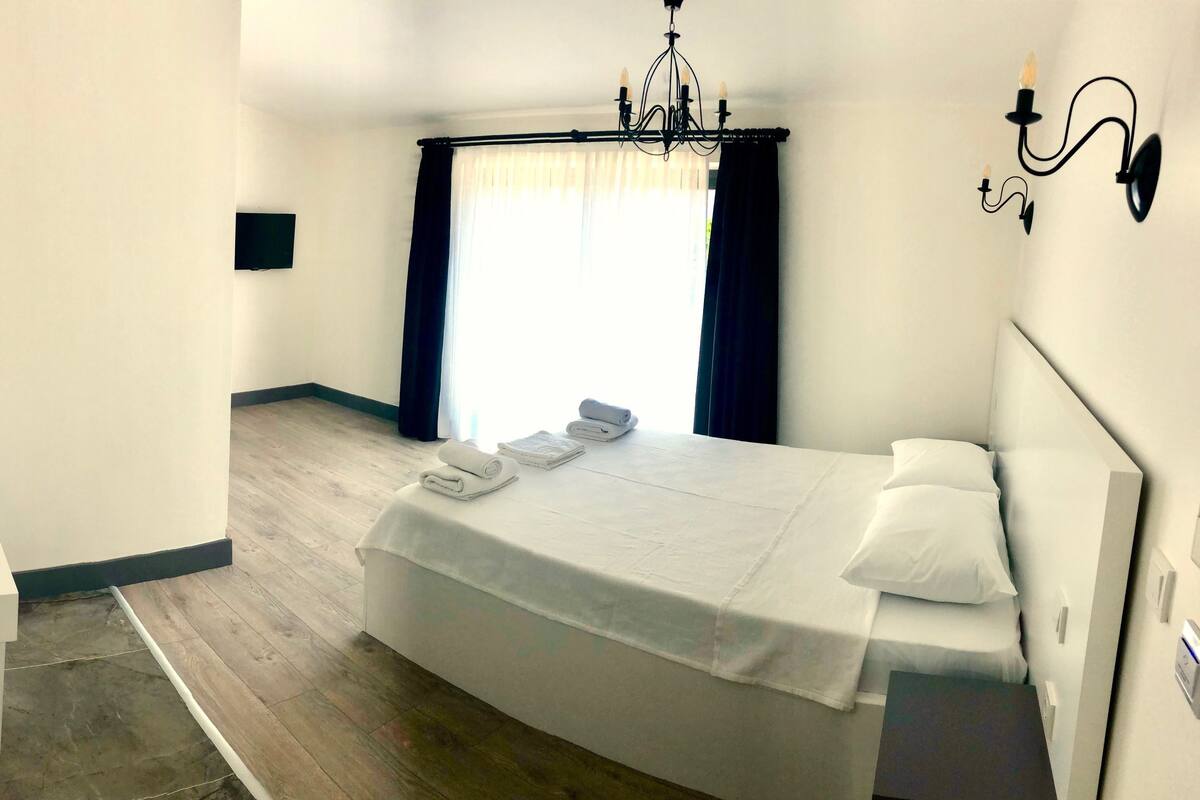 A hotel room with a bed, bedside table, and a large window with curtains.
