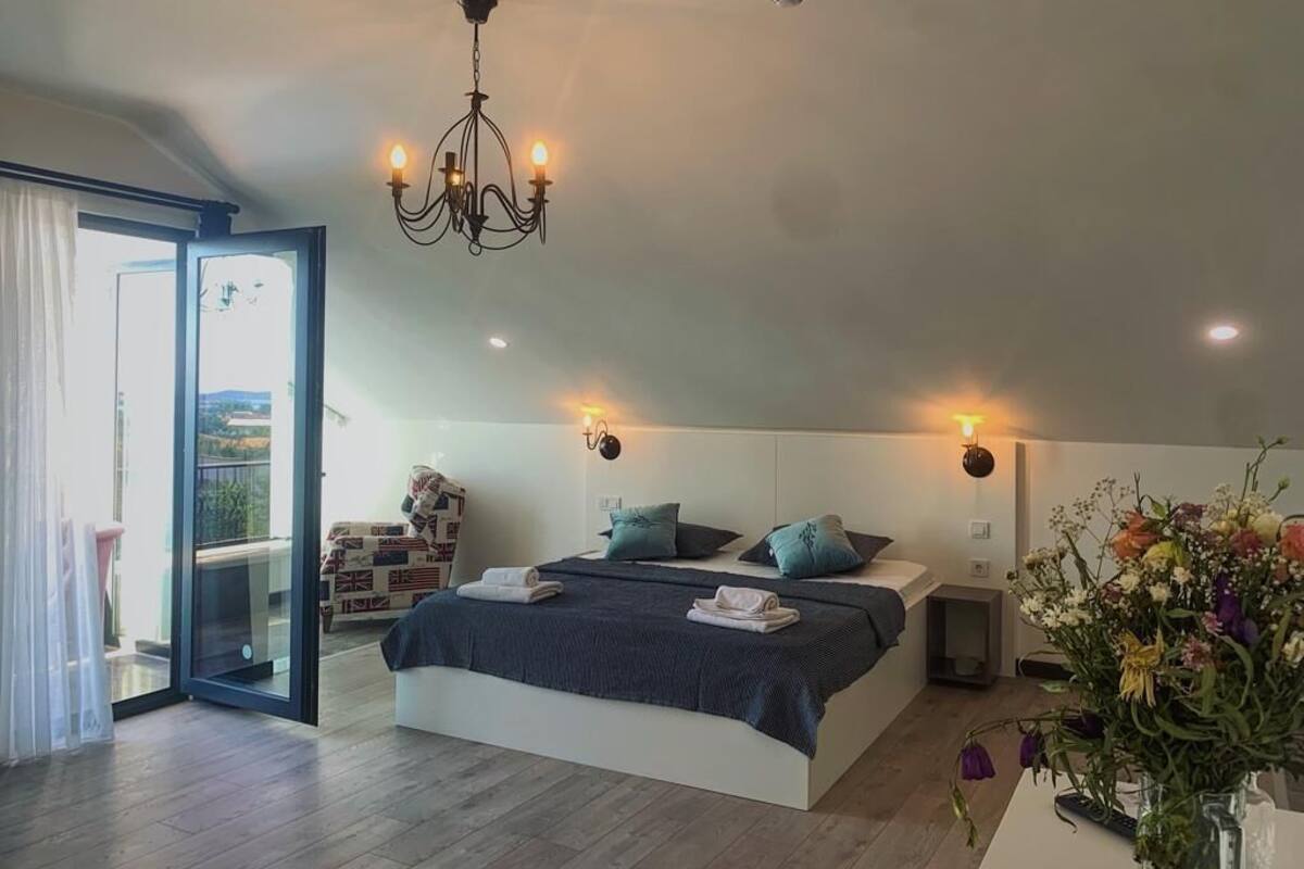 A modern bedroom with a large bed, a chandelier, and a view of the outdoors.