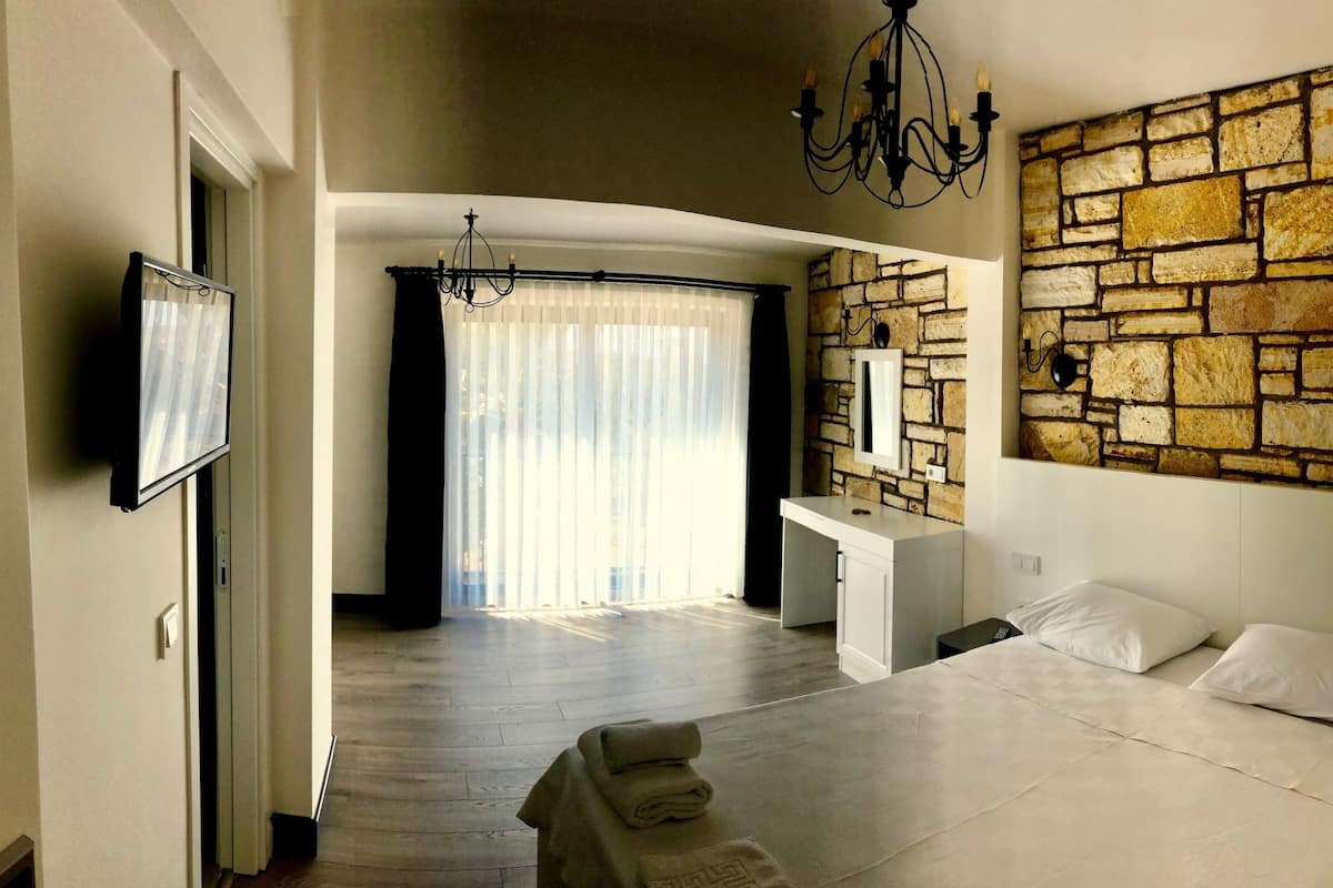 A bedroom with a stone wall, a bed, a desk, and a chandelier.