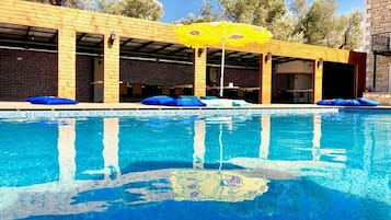 Una piscina con agua azul, rodeada por una terraza de madera y cojines azules.