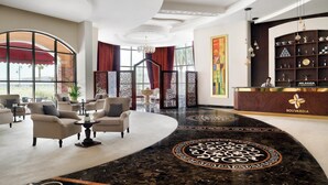 A lobby with a curved marble floor, seating area with armchairs, a reception desk, and a large window with a view. - Crowne Plaza Riyadh Al Waha by IHG (Riyadh)