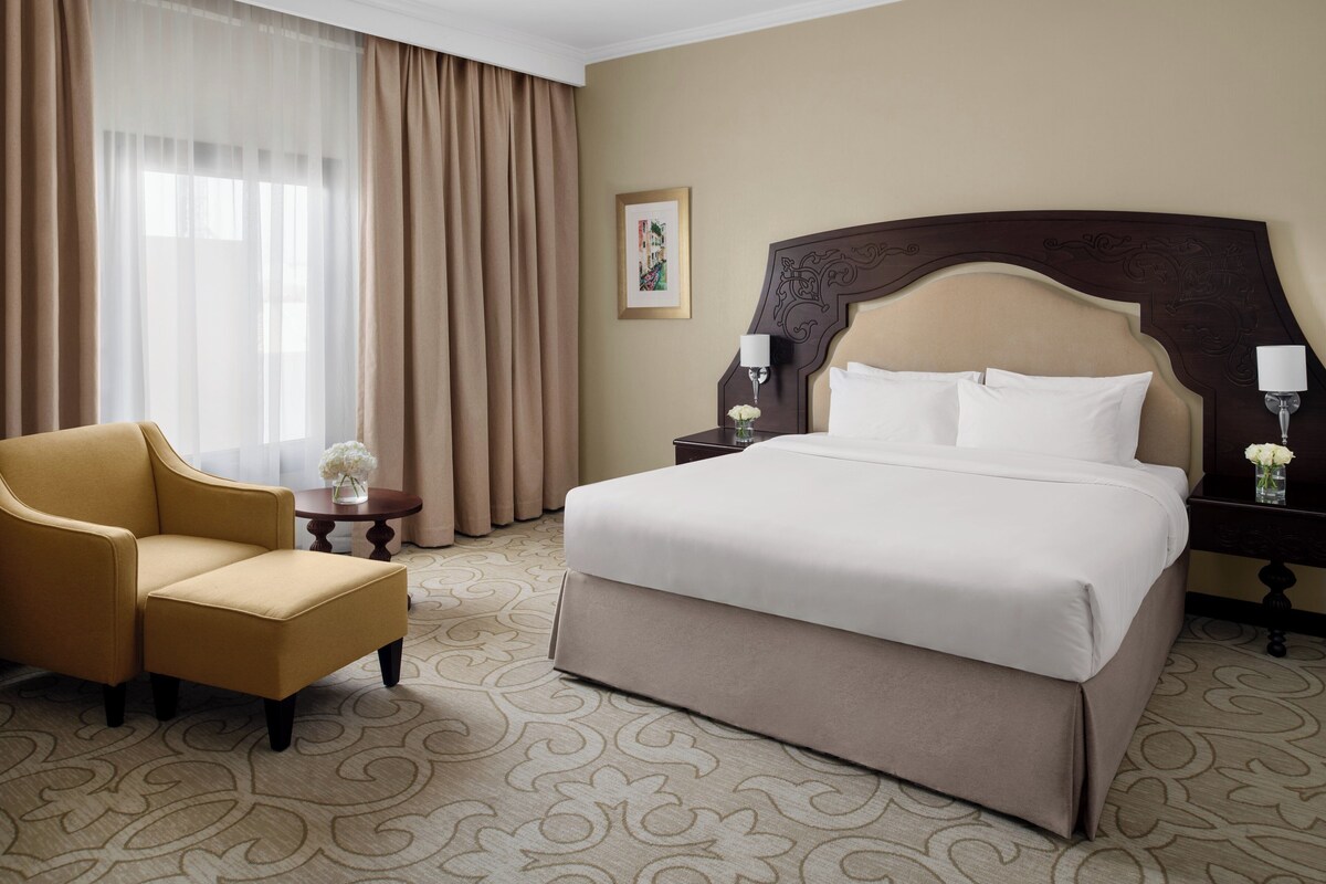 Een hotelkamer met een bed, een stoel, een nachtkastje en een raam met gordijnen.