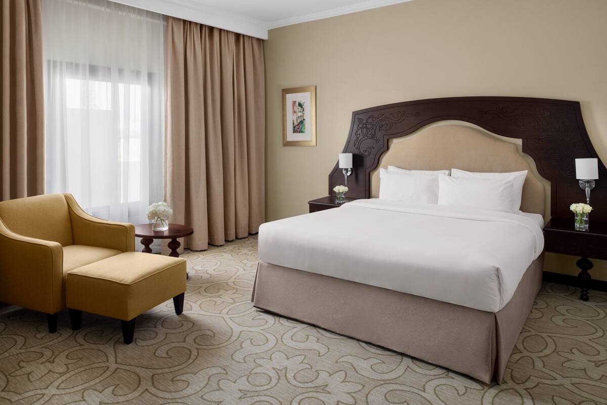 A hotel room with a large bed, a sofa, a nightstand, and a window with curtains.