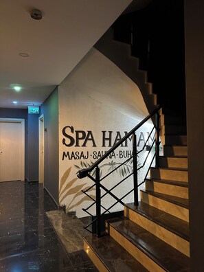 A staircase with a handrail, a wall with the text 'SPA HAM MASAJ SAUNA BUHA', and a door in the background.
