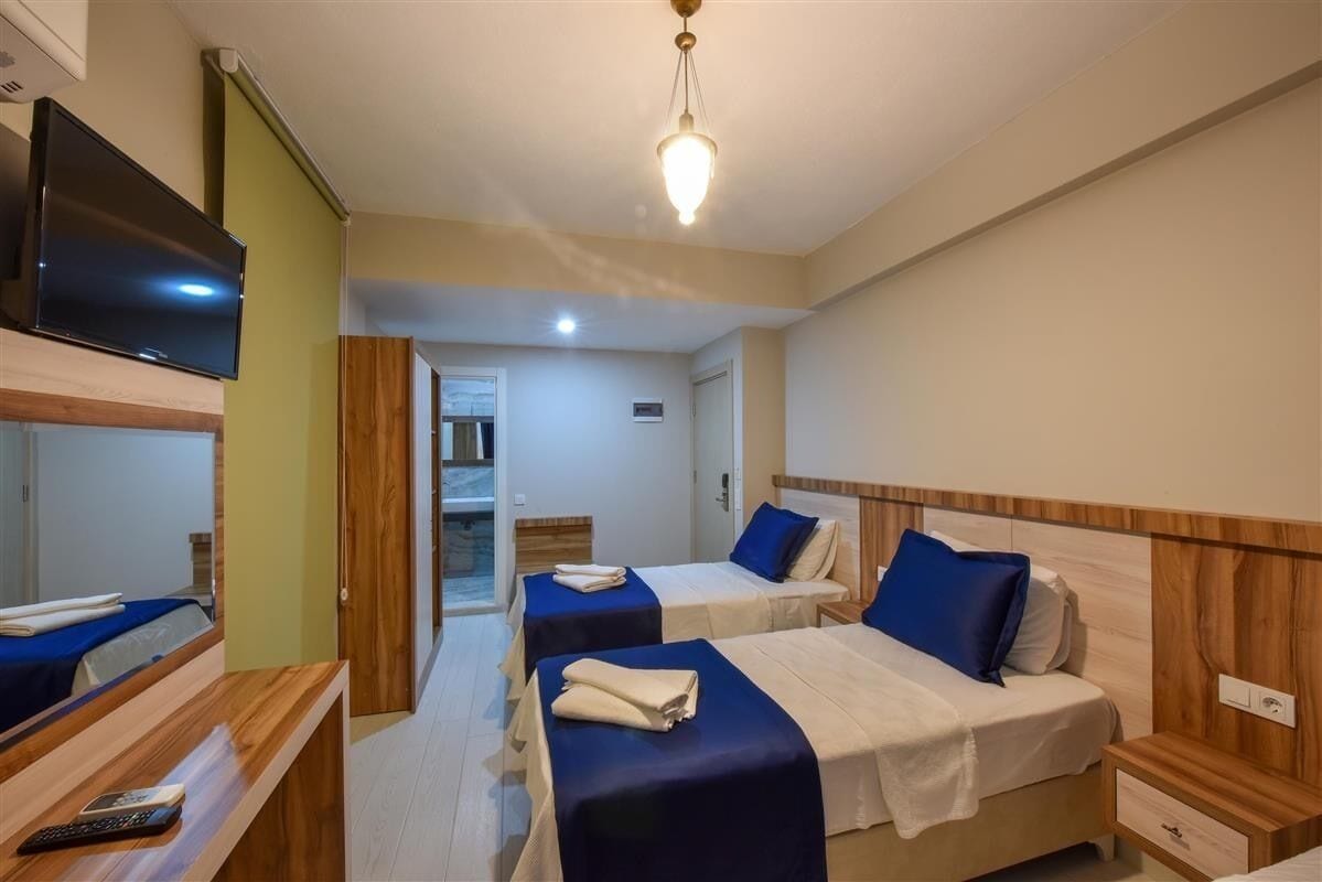 Habitación de hotel con dos camas, televisión, escritorio de madera y baño visible a través de una puerta abierta.