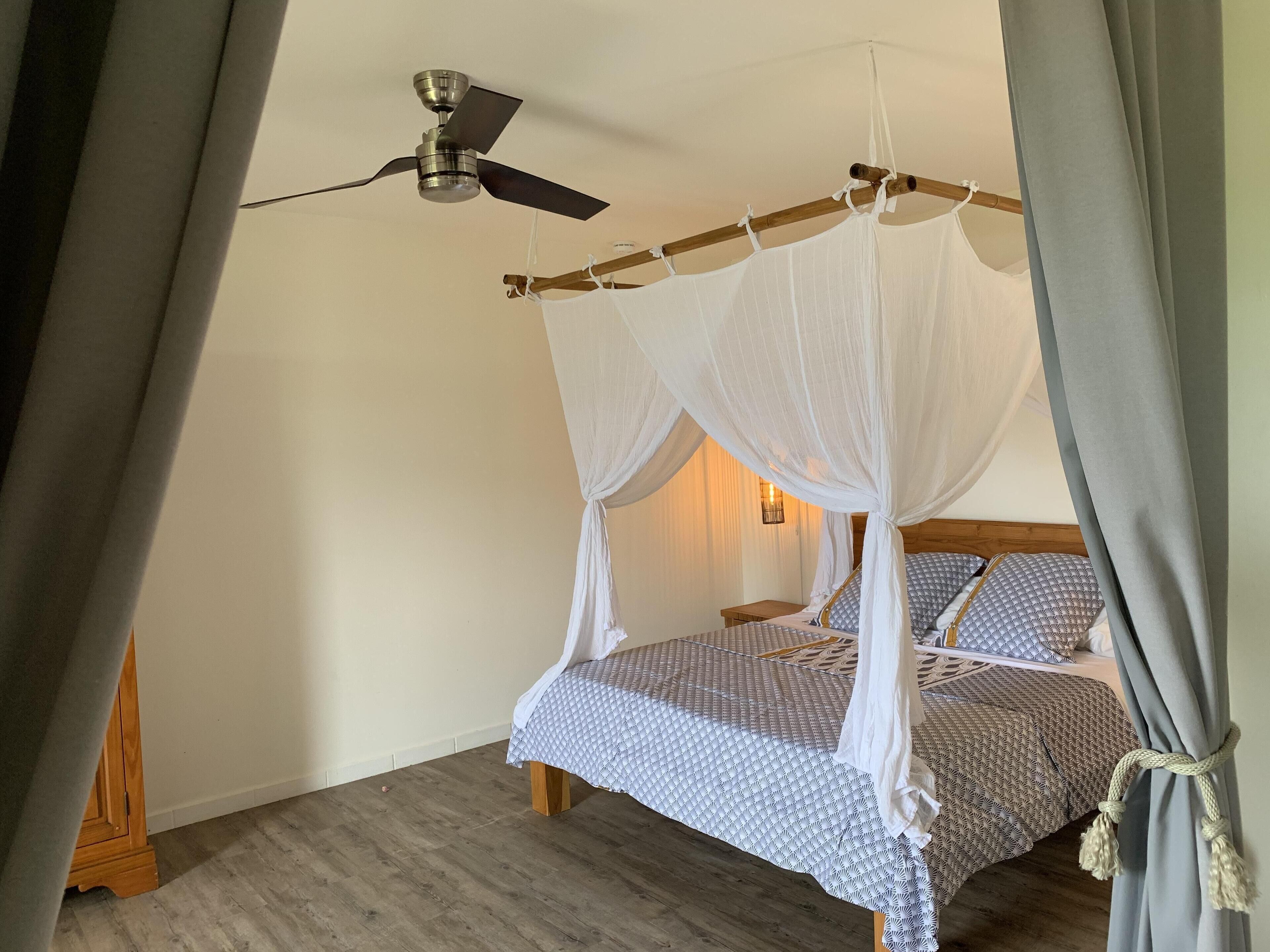 A bedroom with a four-poster bed, a ceiling fan, and a wooden floor.