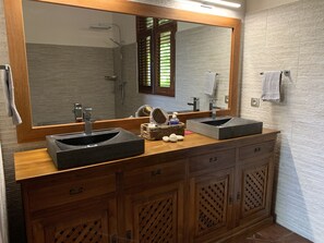 A bathroom with a wooden vanity, two black sinks, a mirror, and a shower.