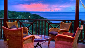 A covered outdoor seating area with wicker chairs and a glass table, overlooking a scenic view of the ocean and greenery. - Between luxury and authenticity.  Beautiful sea view property, 100m from the beach. (Deshaies)