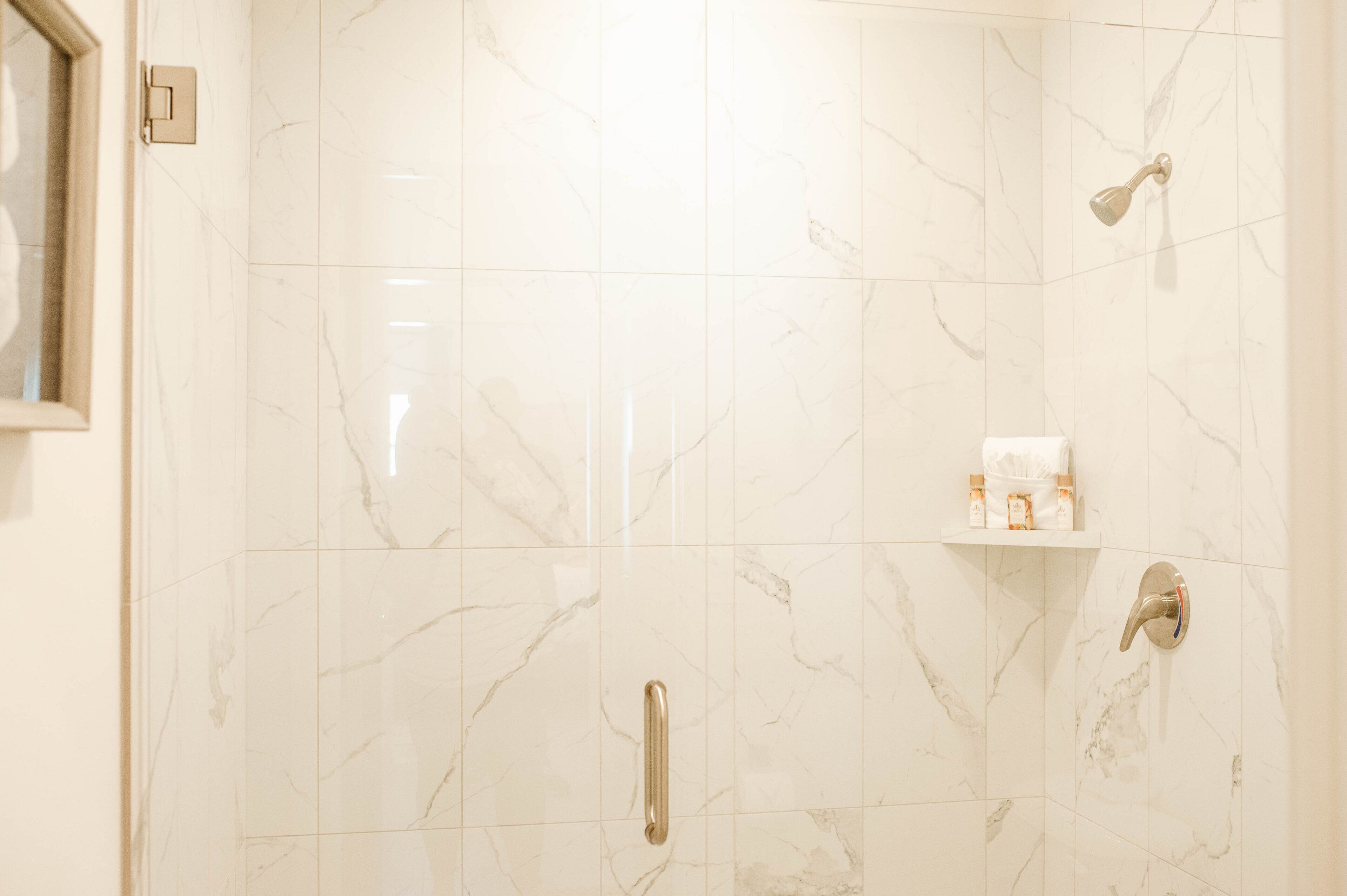 Een badkamer met marmeren tegels, een douche, een toilet en een plank met toiletartikelen.