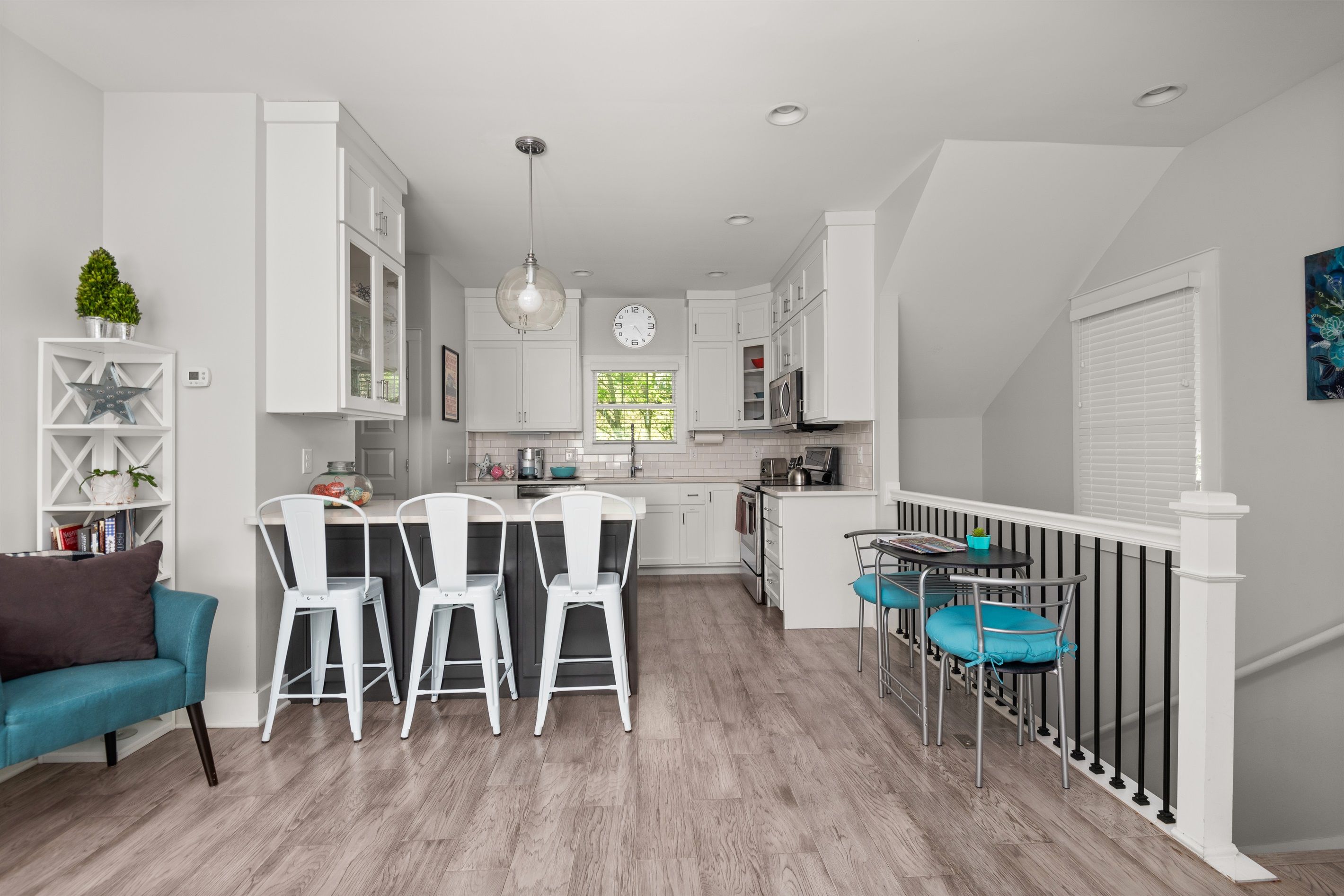 Una cocina moderna con muebles blancos, un comedor con sillas blancas y una escalera con barandilla.