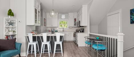 Una cocina moderna con muebles blancos, un comedor con sillas blancas y una escalera con barandilla.