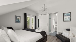 Ein Schlafzimmer mit einem großen Bett, einer Bank, einer Chandelieber und einer Tür zu einem Badezimmer.