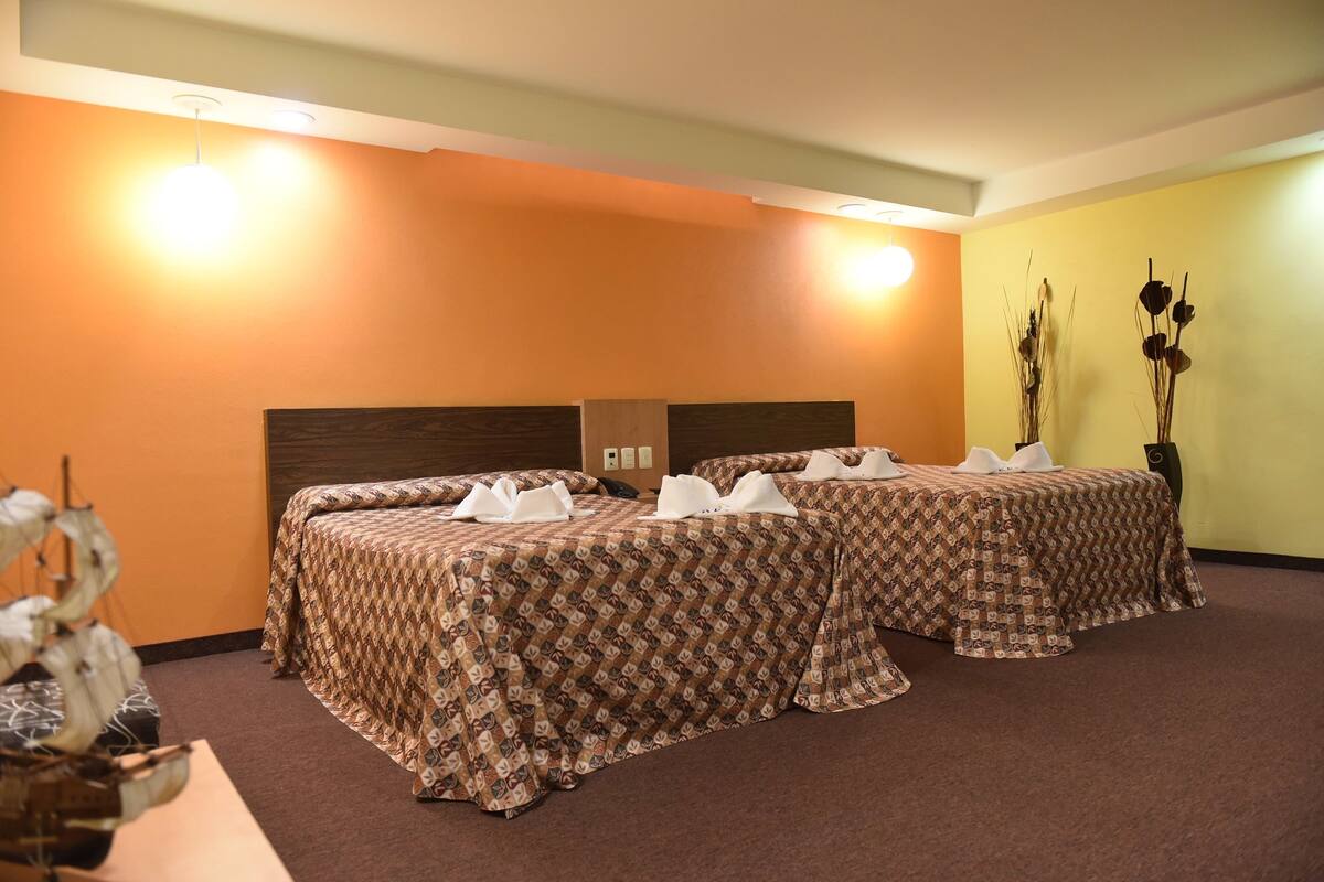 A hotel room with two beds, each with a patterned bedspread and white towels.