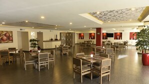 Un restaurante espacioso con varias zonas de comedor, mesas y sillas de madera, y un diseño de techo moderno.