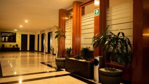 Un vestíbulo de hotel con piso de mármol pulido, paneles de madera y plantas en macetas.