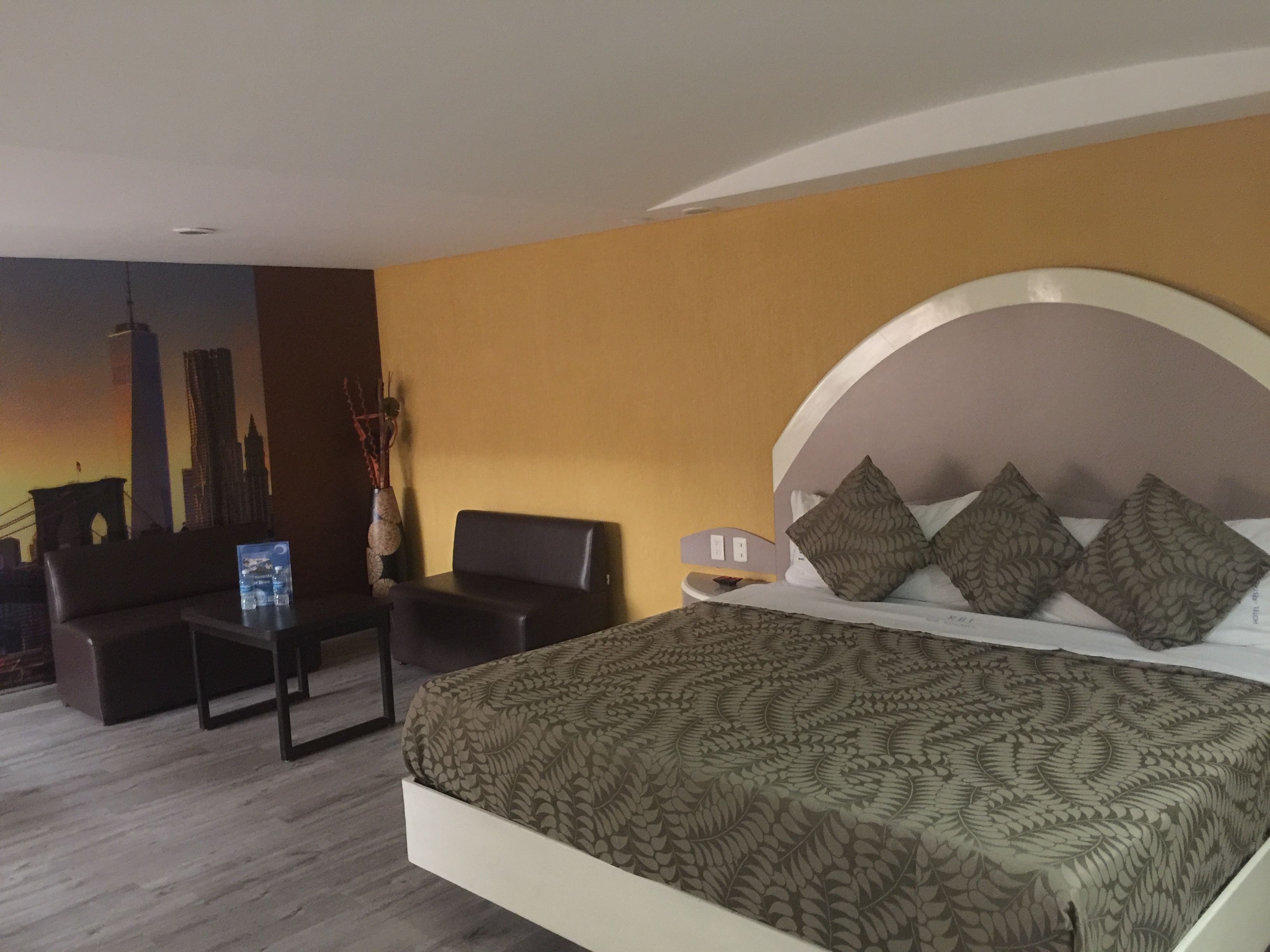 A hotel room with a bed, a desk, a chair, and a cityscape mural on the wall.