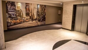 Un vestíbulo de hotel con un gran mural de la ciudad en la pared, suelo de mármol y un ascensor.