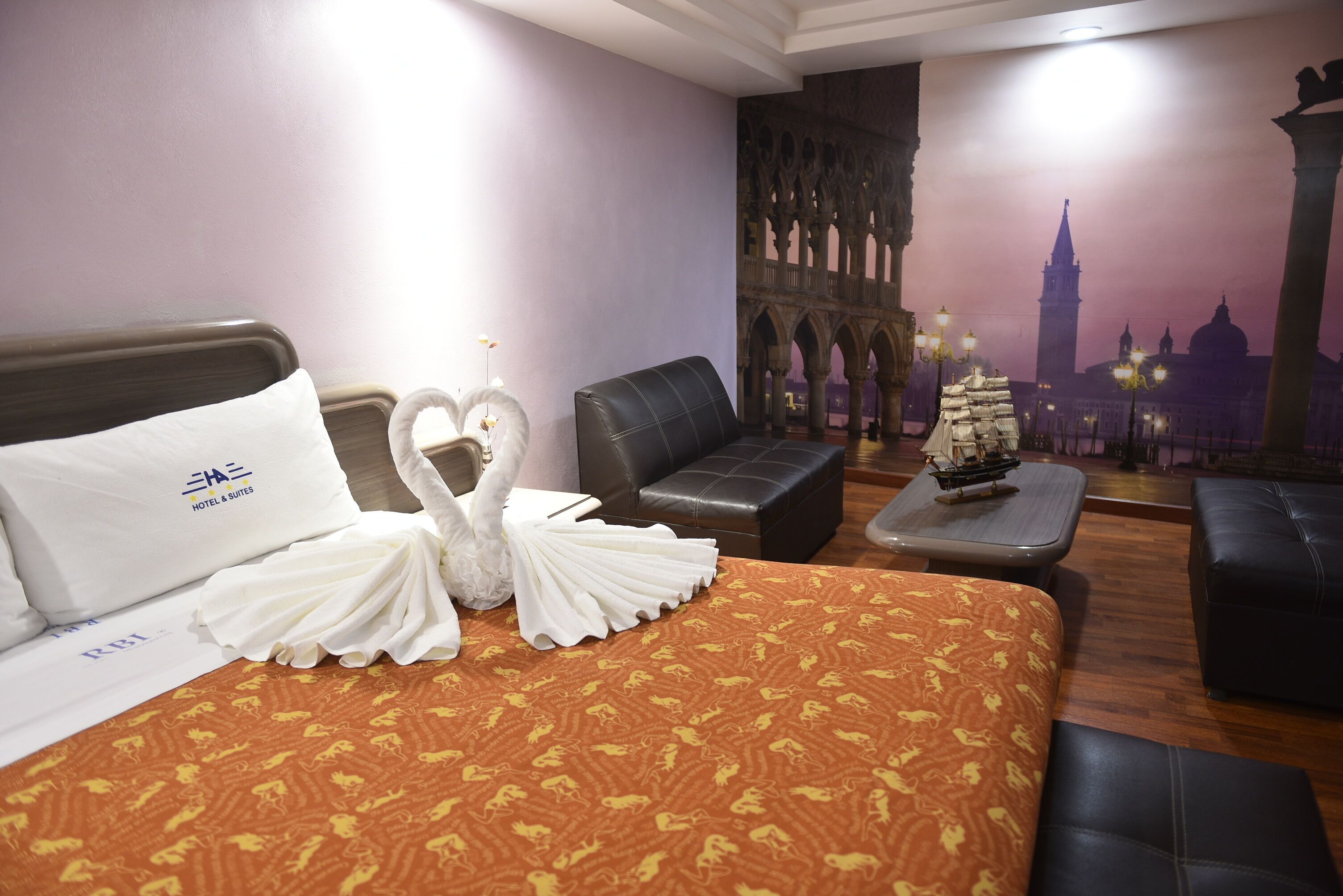 Ein Hotelzimmer mit Bett, einer Couch, einem kleinen Tisch mit einem Schiffmodell und einem Wandgemälde einer Stadtansicht.
