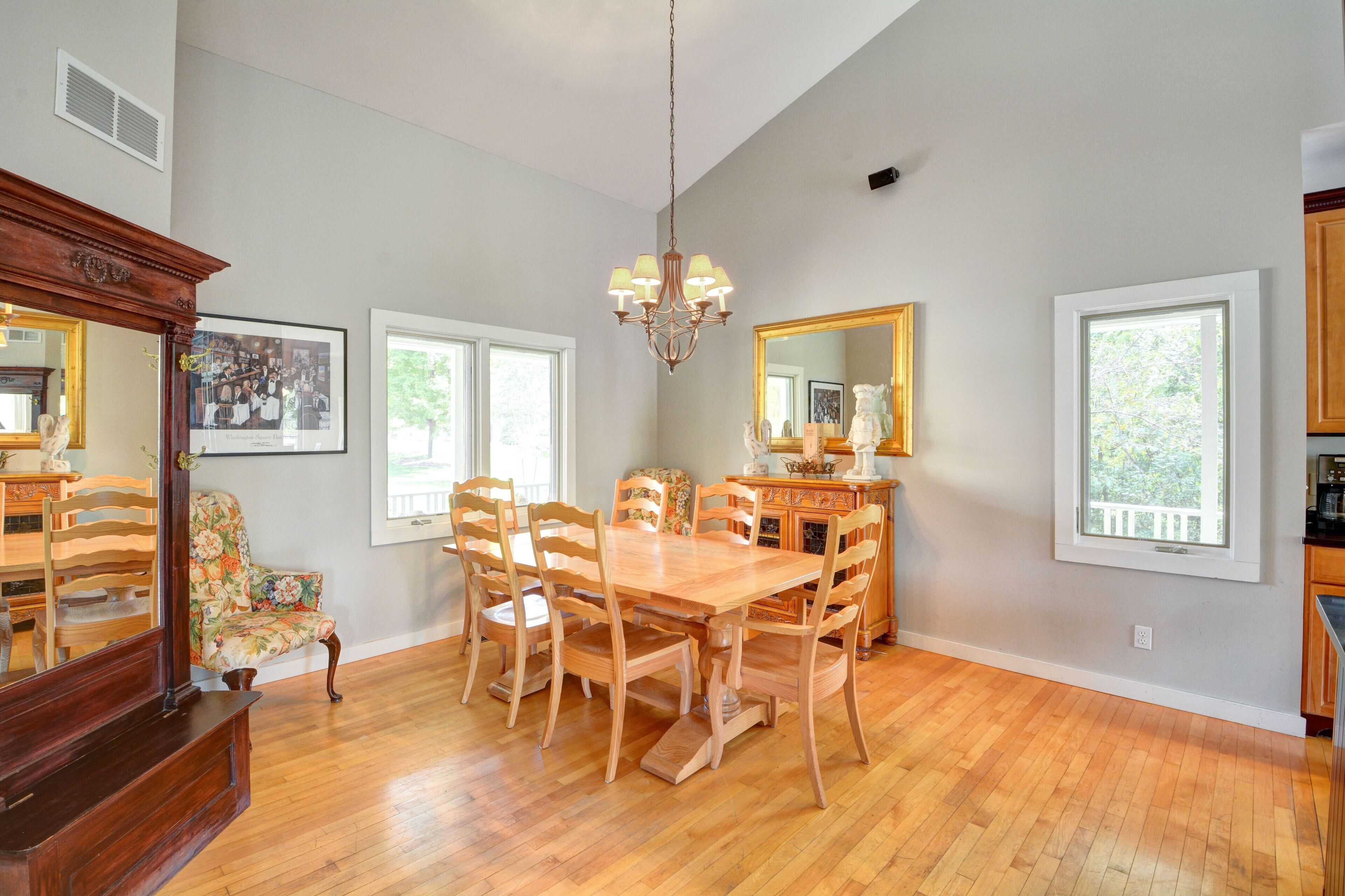 A dining room with a wooden table and chairs, a chandelier, a floral armchair, and a large mirror on the wall.
