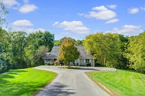 Une maison à deux étages avec une allée menant à un garage, entourée de pelouses verdoyantes et d’arbres.
