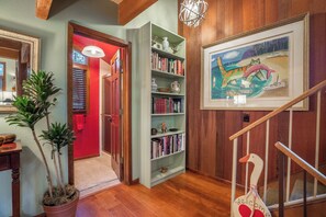 A hallway with a wooden staircase, a bookshelf, a potted plant, and a painting on the wall.