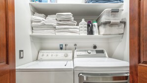 Une buanderie équipée d’un lave-linge et d’un sèche-linge à chargement frontal, d’une étagère avec des serviettes pliées et d’une autre étagère avec des produits de lessive.