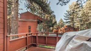 Une terrasse en bois dotée d’un espace abrité, offrant une vue sur une zone boisée où se trouvent plusieurs cabanes.