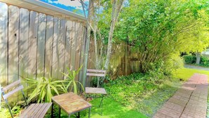 Une clôture en bois, deux tables en bois et un chemin pavé de briques dans un jardin.