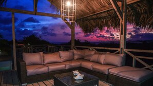 An outdoor seating area with a wicker sofa and a coffee table, under a thatched roof structure. - Hakuna Matata Bonaire (Kralendijk)