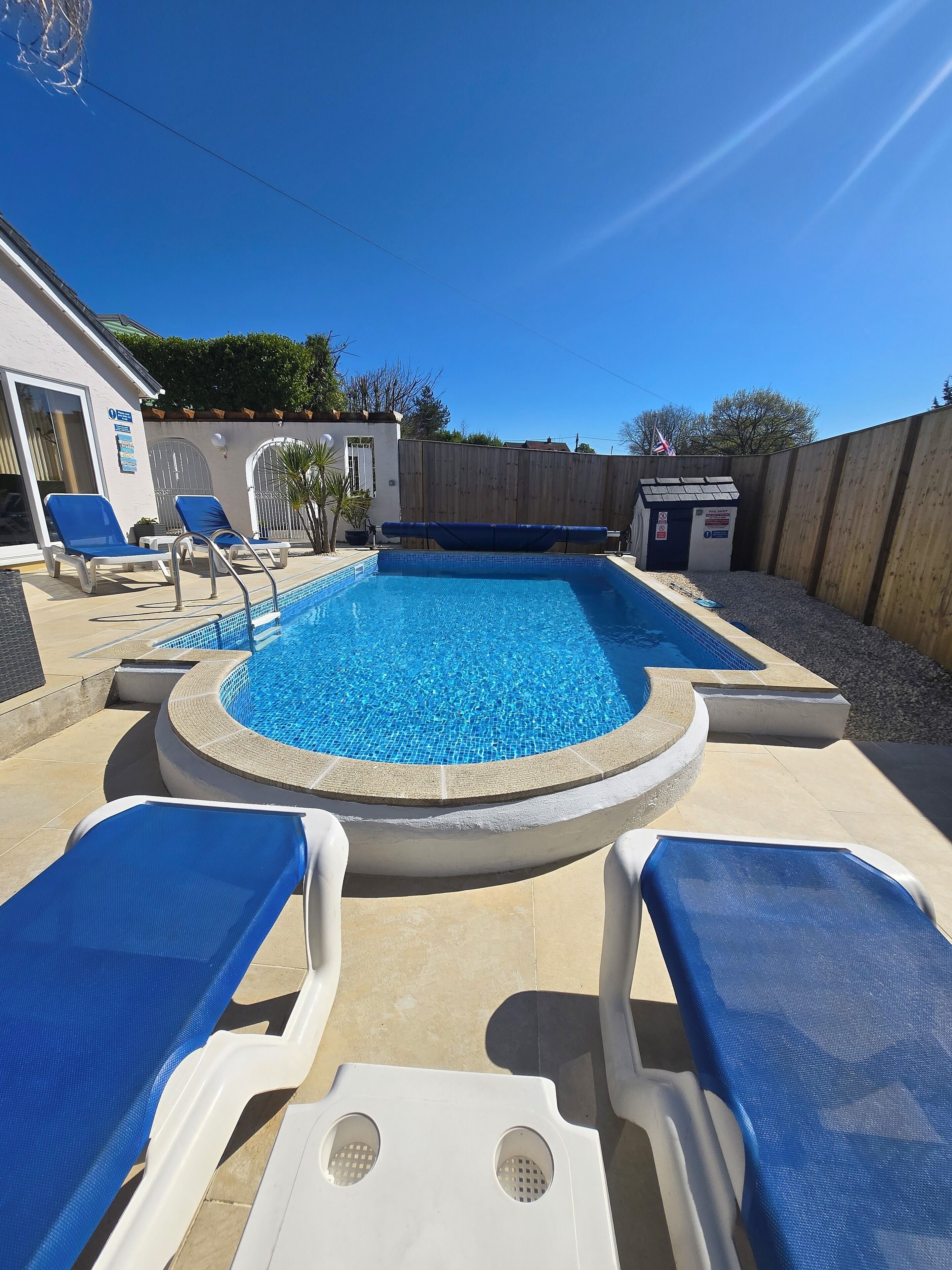 Ein Swimmingpool mit blauen Fliesen, umgeben von einem Holzzaun und einem weißen Gebäude.
