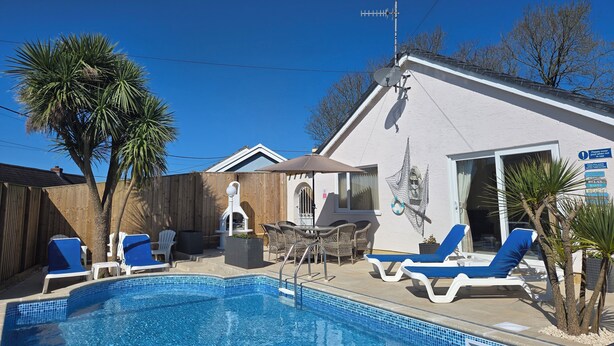 Ein Swimmingpool mit Liegestühlen, eine Terrassenanlage und ein Gebäude mit Satellitenschüssel.