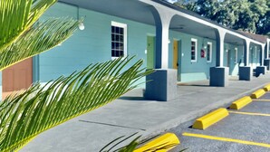 Fila de habitaciones de motel con estructura de un piso, cada una con puerta y ventana, y un estacionamiento con bordes amarillos.