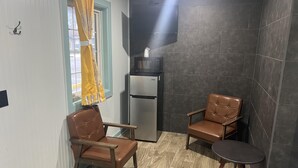 Una habitación pequeña y bien iluminada con dos sillones de cuero, una mesa pequeña, un refrigerador y un televisor montado en la pared.
